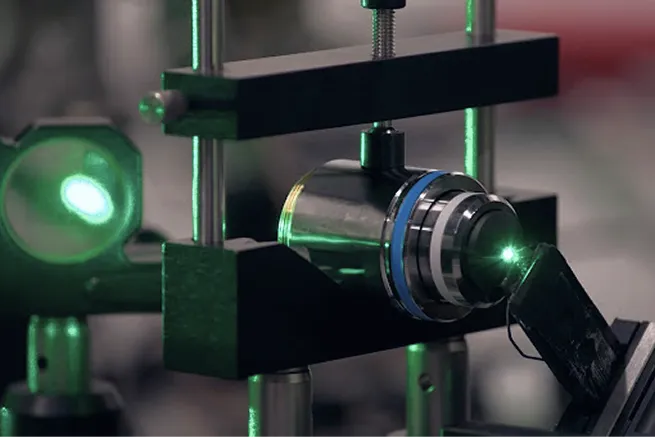Close-up of laboratory laser apparatus emitting a green light beam through optical components.