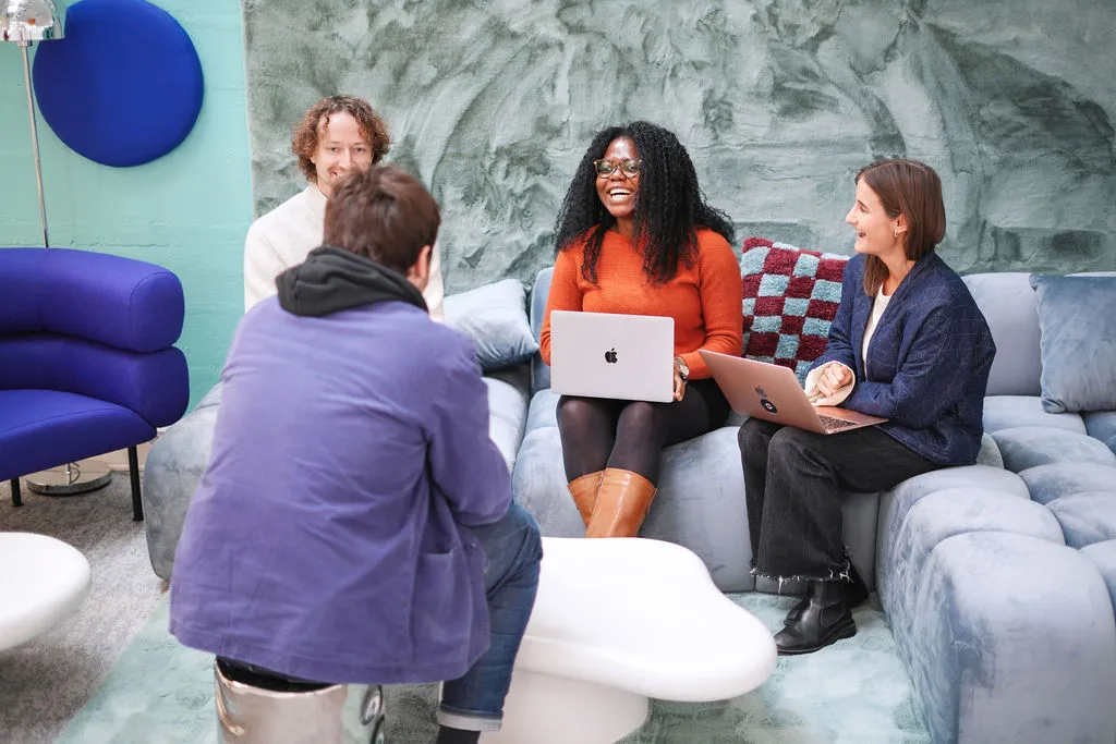 Two women sitting on a light blue couch in a modern room with a teal wall, gray abstract artwork, and circular blue decorations.
