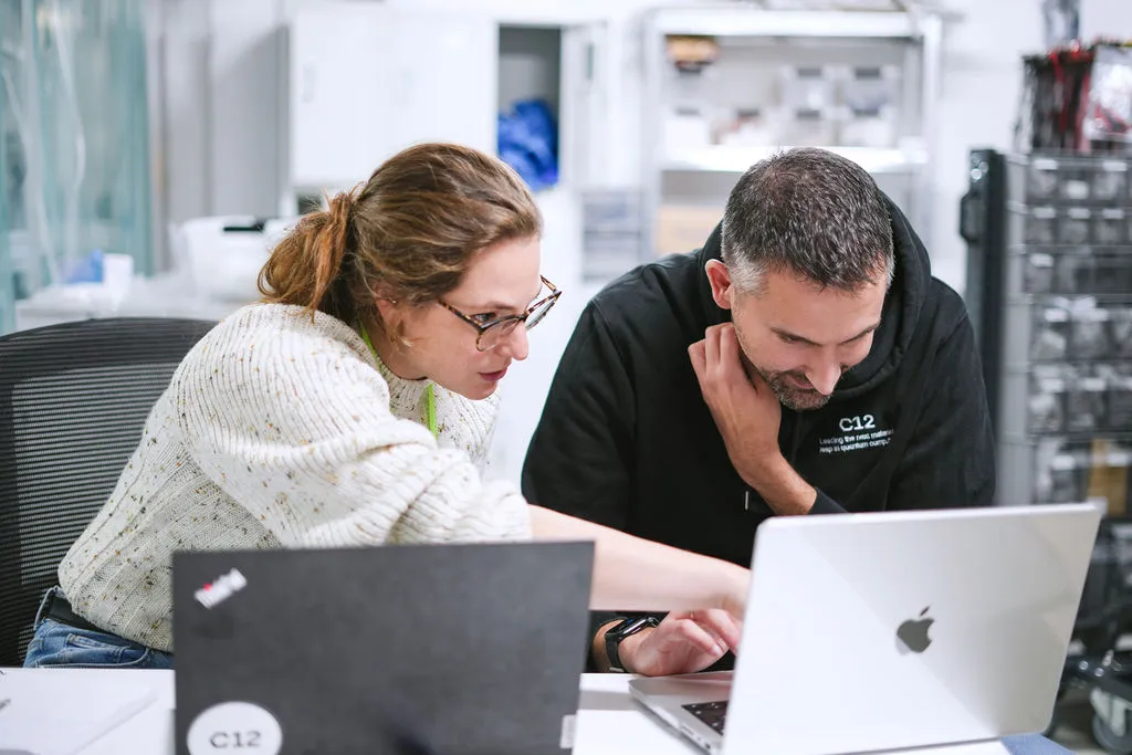 Scientist in blue protective gear and gloves working at a computer in a laboratory with scientific equipment.