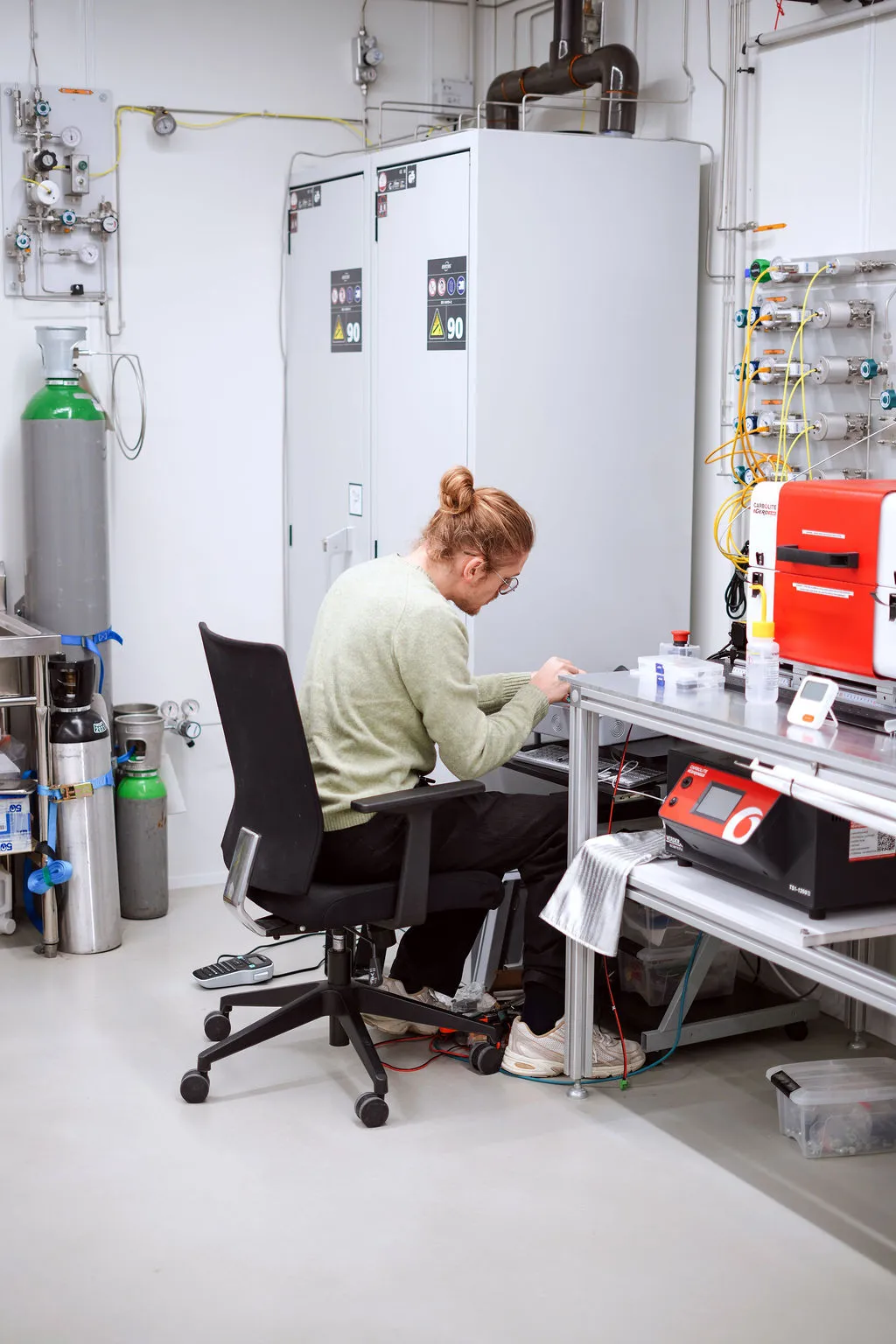 Two scientists in blue lab coats working with laboratory equipment and computer screens in a clean, white lab.