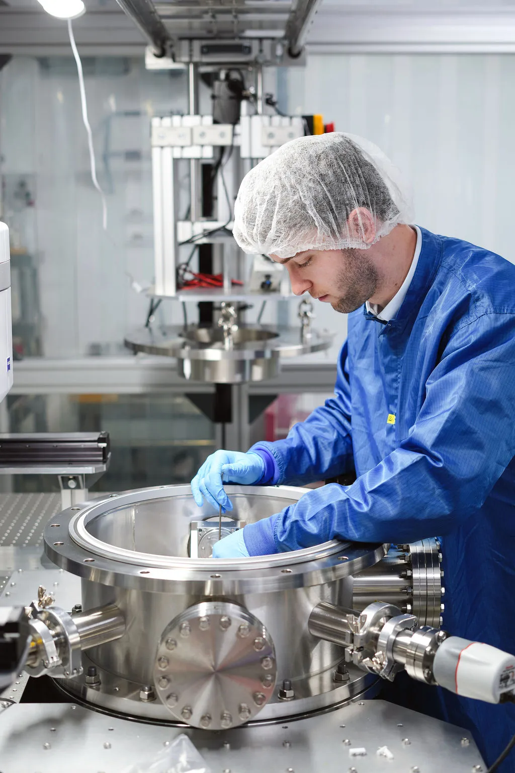Gloved hand using a wrench to tighten a bolt on a stainless steel industrial valve in a laboratory setting.