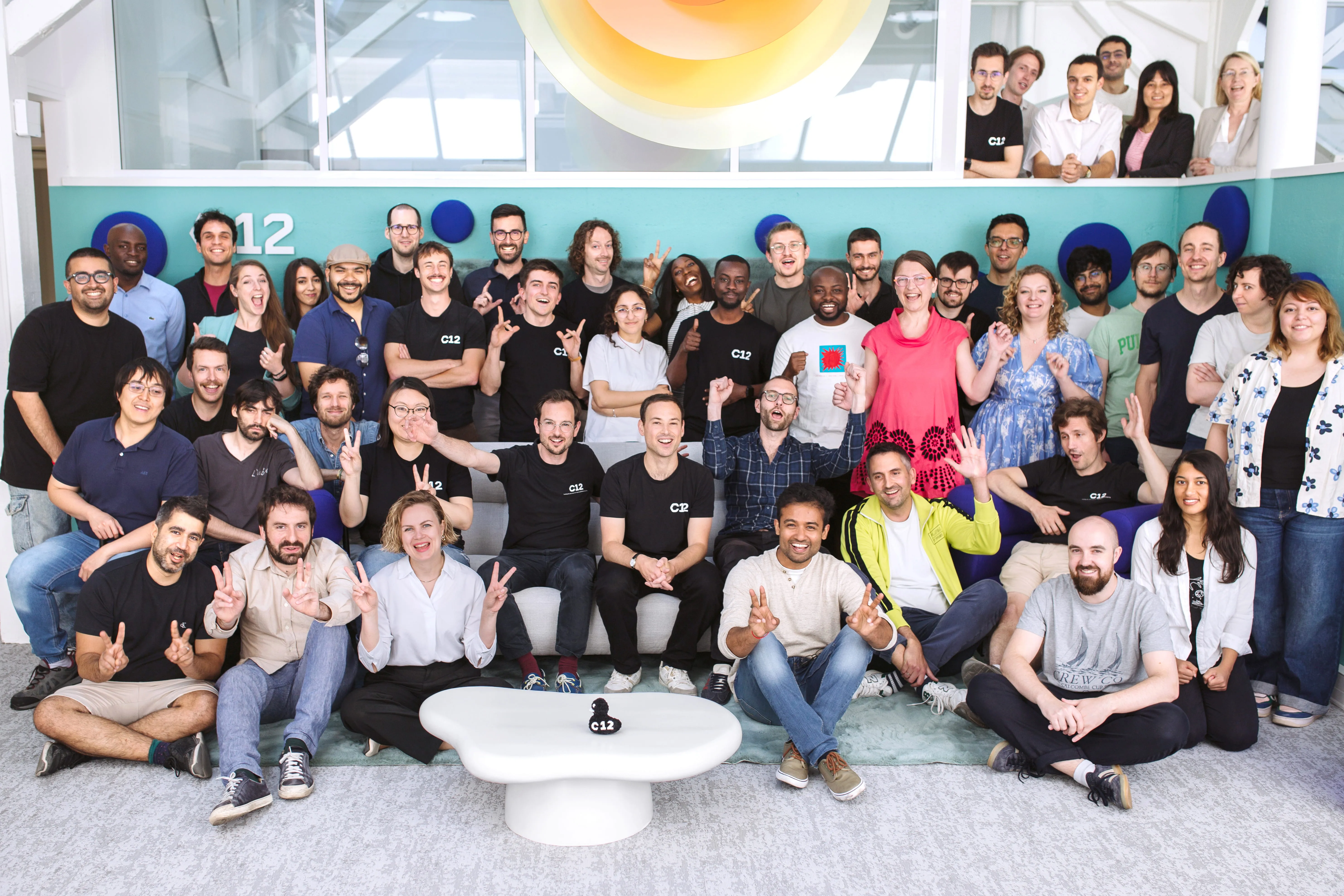 Large diverse group of people posing together indoors against a turquoise wall with white modern decor.