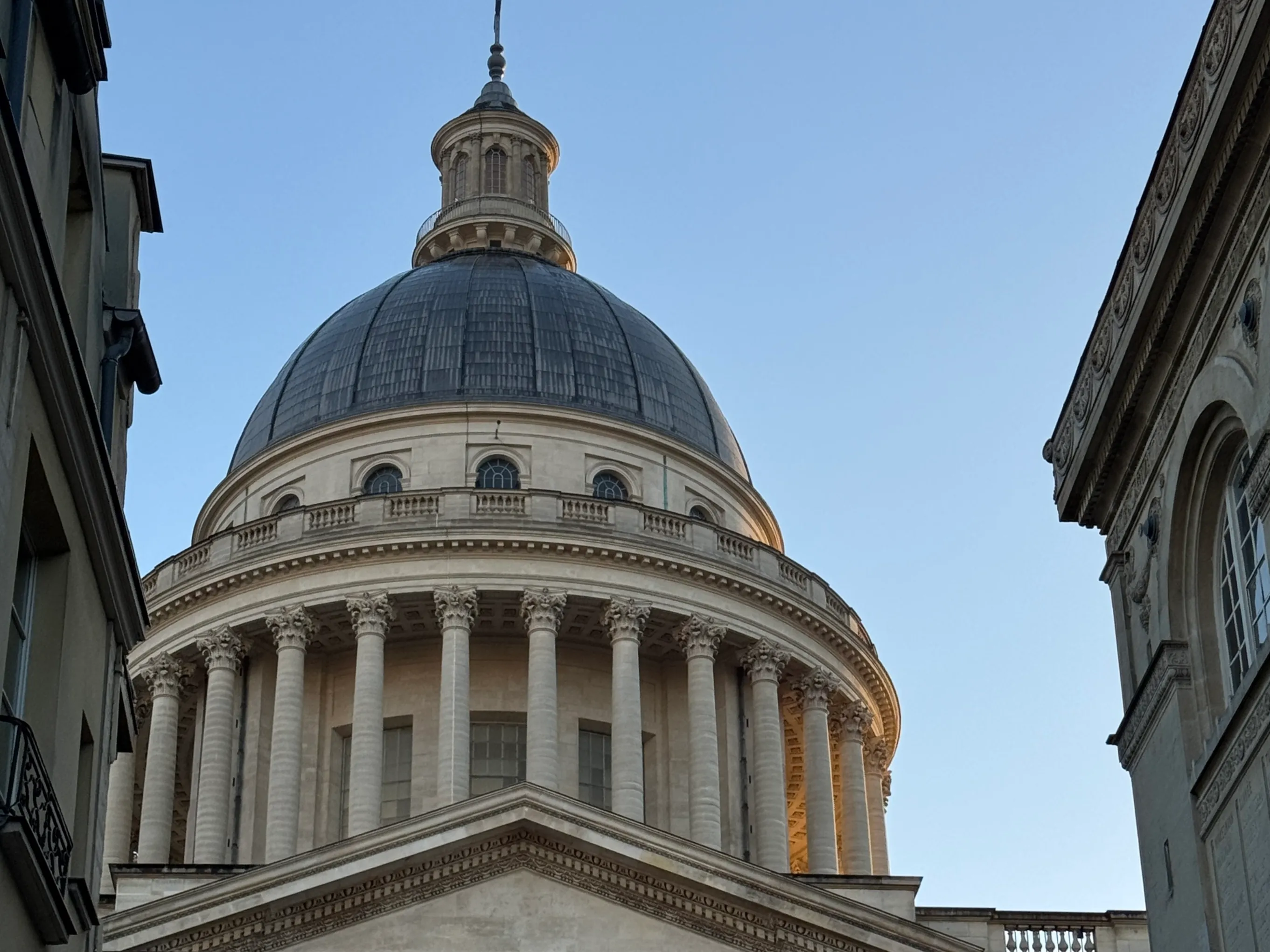 Street view of historic buildings leading to a large domed neoclassical building with columns.