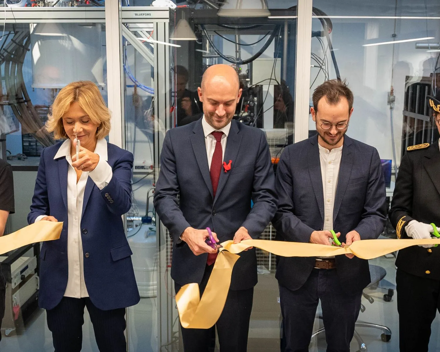 Five people in formal and casual attire cutting a ceremonial ribbon indoors.