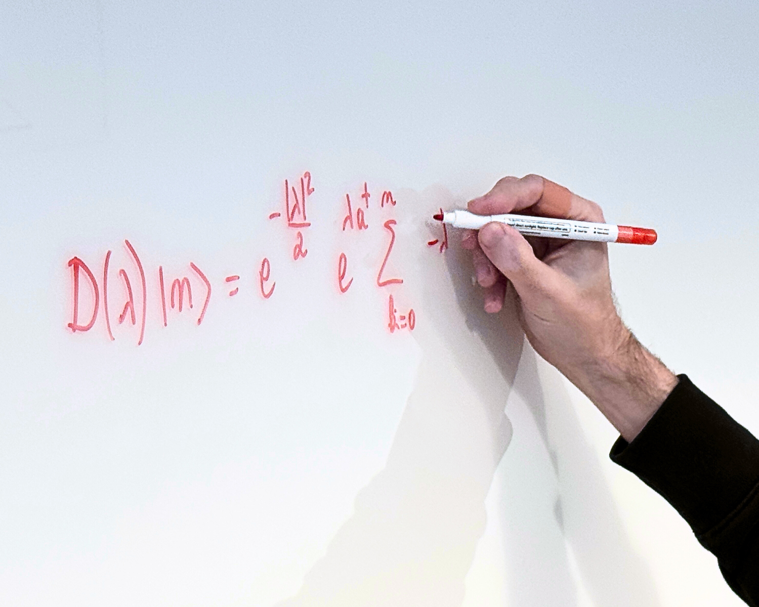 Two men collaborating at a whiteboard, one writing with a marker while the other observes.