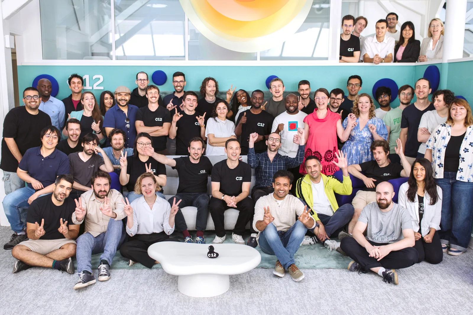 Large diverse group of people posing together indoors against a turquoise wall with white modern decor.