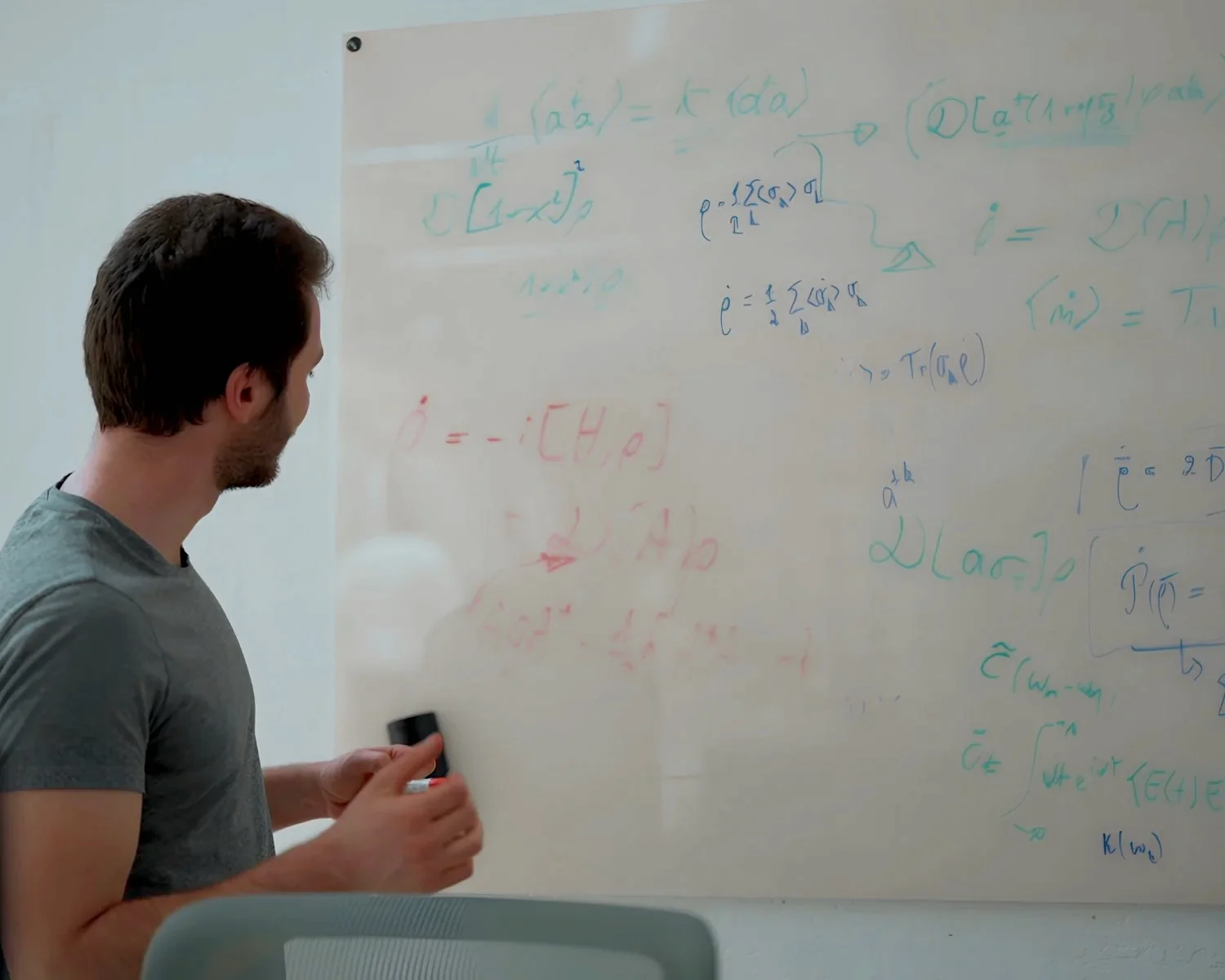 Two men collaborating at a whiteboard, one writing with a marker while the other observes.