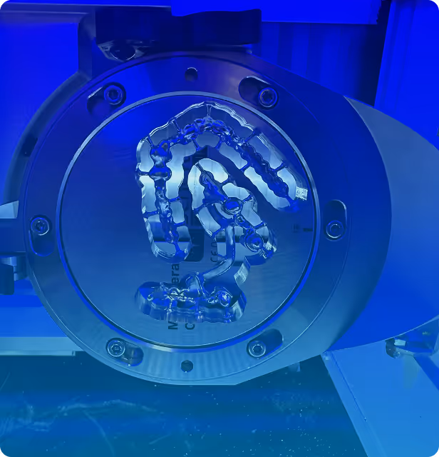 Close-up of a transparent dental aligner mold on a circular metal platform illuminated by blue light.