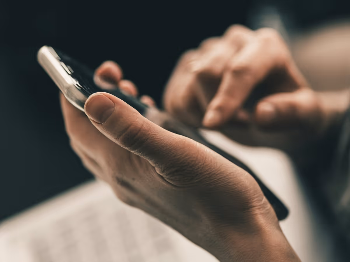 Close-up of hands holding and using a smartphone with a dark background.