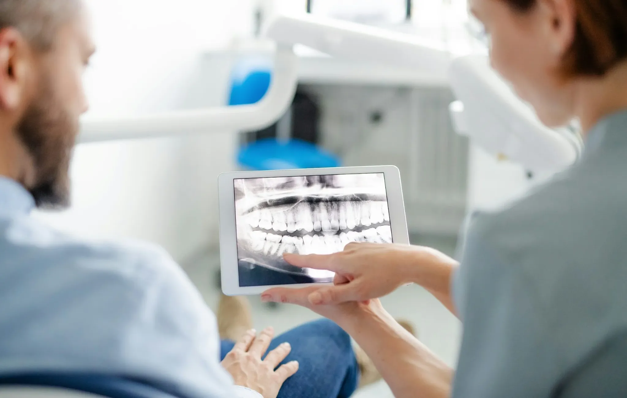 Female dentist wearing a mask showing a dental X-ray to a male patient seated in the dental chair.