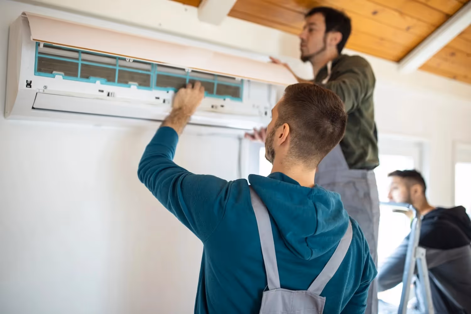 HVAC technicians installing or servicing a ductless mini-split AC unit indoors.