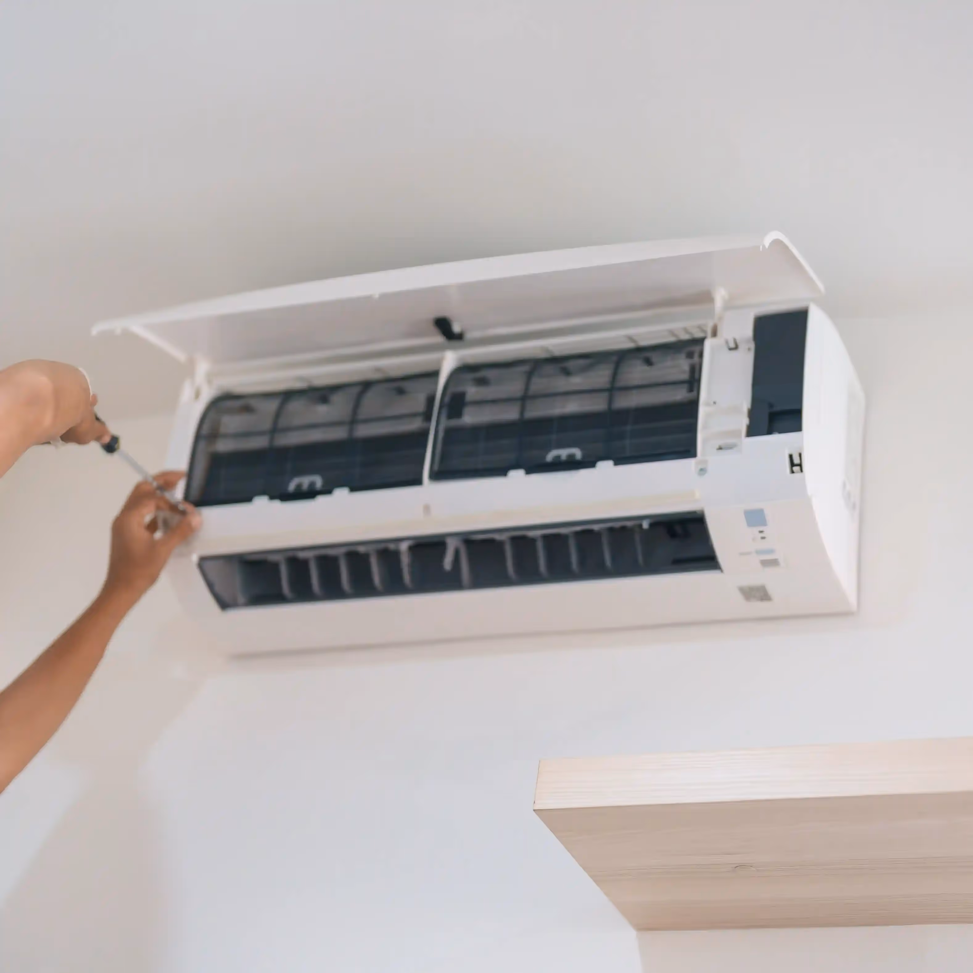 A person's hands are using a screwdriver to work on a wall-mounted air conditioner.