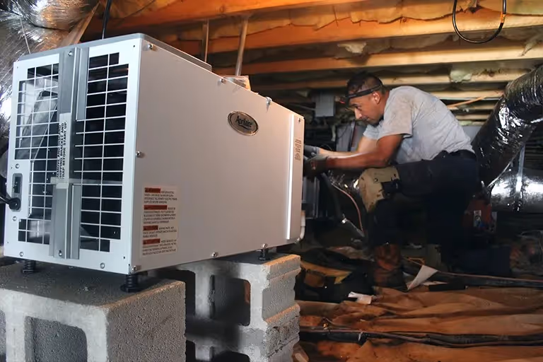 Technician installing dehumidifier in low crawlspace.