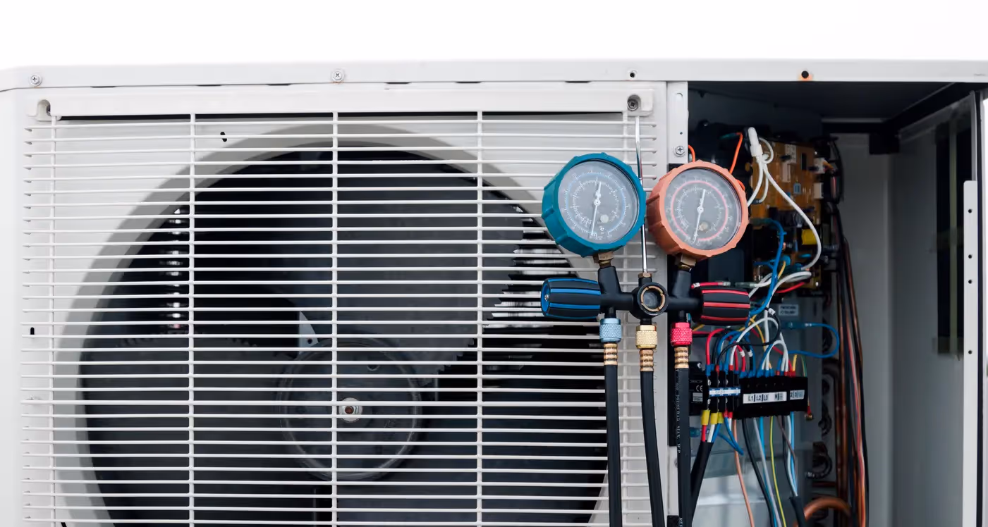 Outdoor AC condenser unit with fan grille and open panel shows wiring and pressure gauges during service.