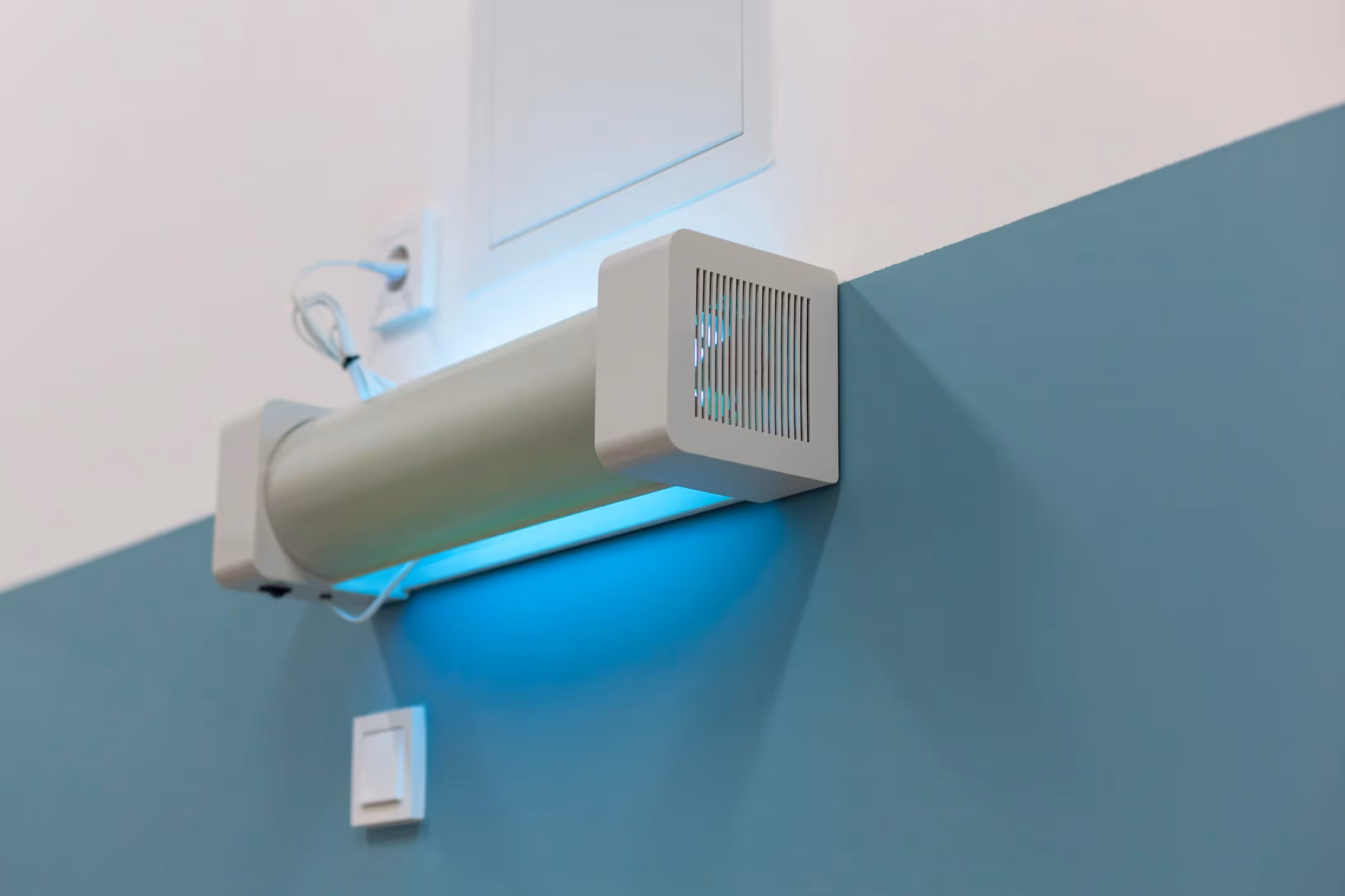 Wall-mounted UV-C air purifier glowing blue, used for indoor air sterilization in public or medical spaces.