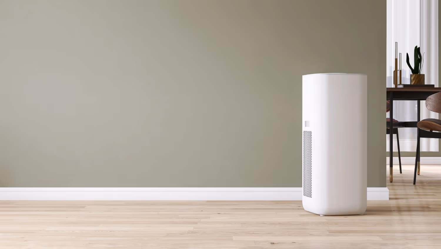 A high-angle view of a white tower air purifier with a square body and a circular spoke-patterned top vent, positioned on a light wood floor next to a green leafy plant.
