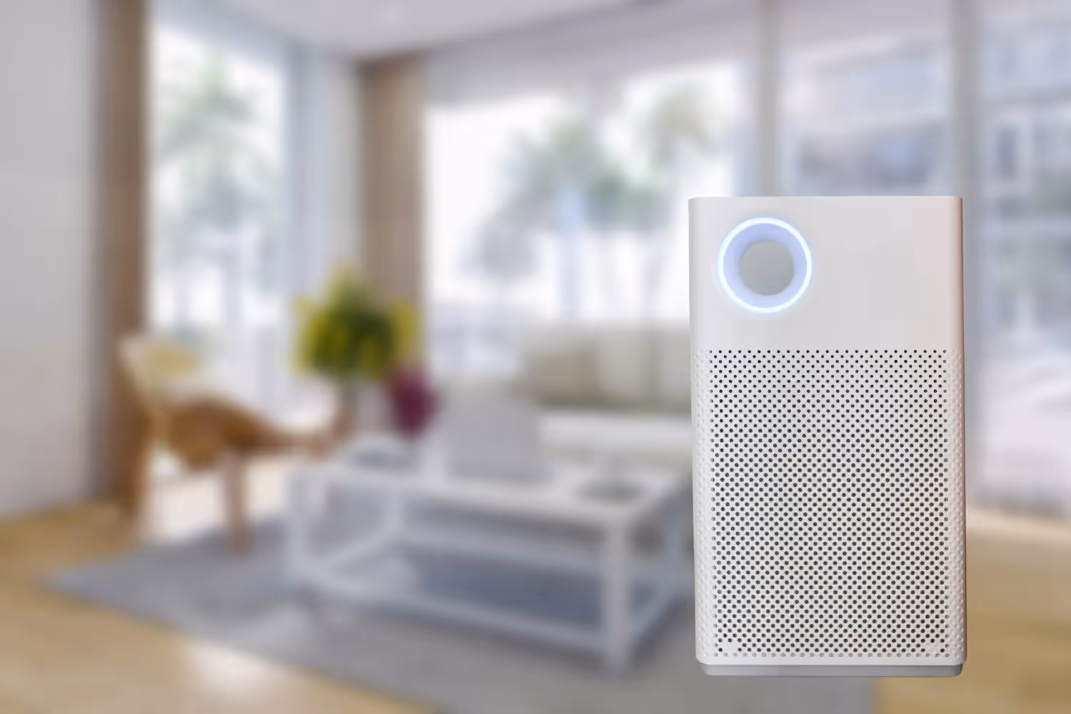 A white tower air purifier with a perforated intake base and a circular LED light ring on the front panel. It is shown against a bright, blurred living room background.