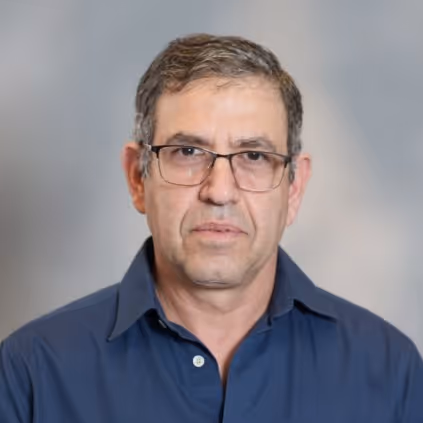 Middle-aged man with short graying hair and glasses wearing a dark blue collared shirt against a blurred gray background.