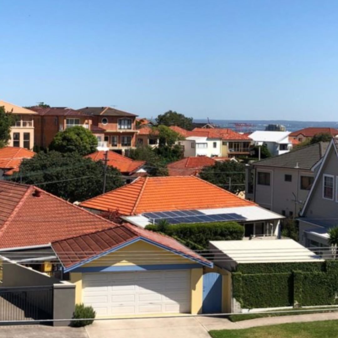 Neighborhood view with houses featuring red and brown tile roofs under a clear blue sky.