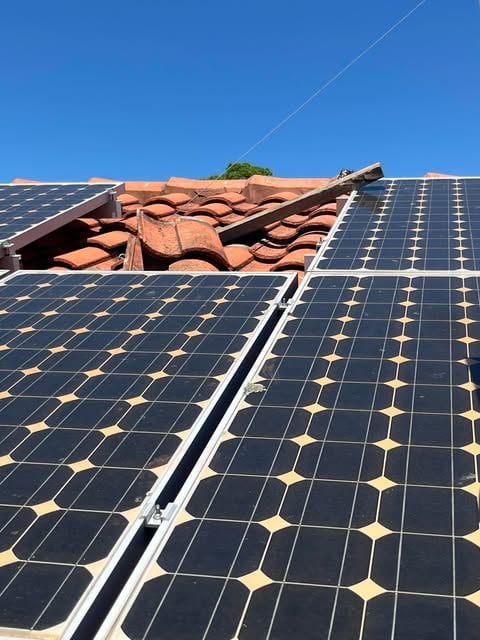 Close-up view of solar panels installed on a terracotta tiled roof under a clear blue sky.