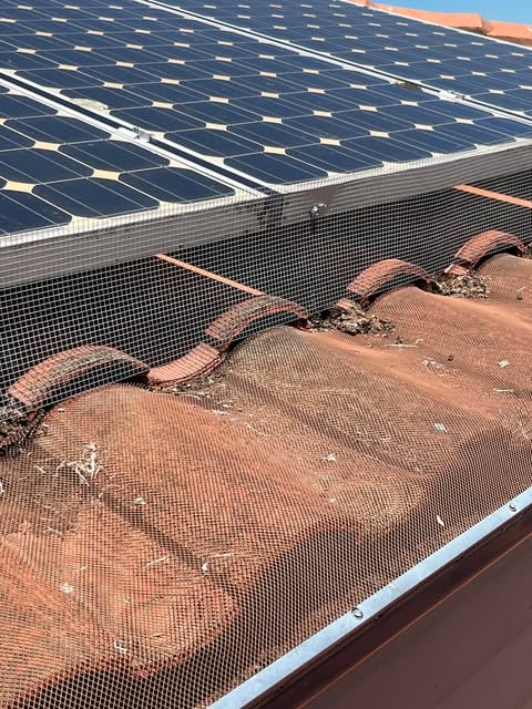 Solar panels installed above terracotta roof tiles with a fine mesh screen covering the gap to prevent debris accumulation.