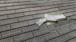 Shingled roof with damaged and displaced grey asphalt shingles exposing the underlayment.