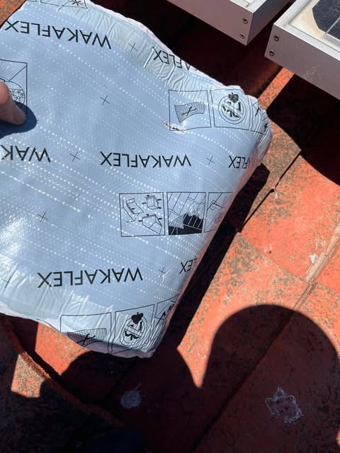 Hand holding a WAKEFLEX branded packaged product on red, sunlit tiles with shadows around.