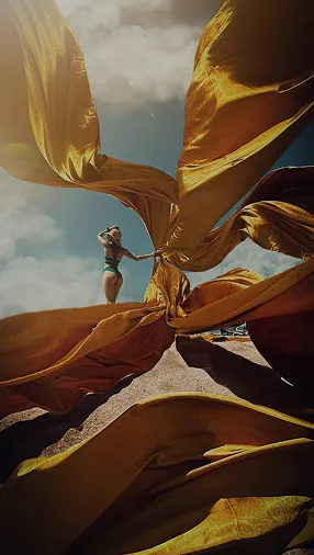 Ефектне фото дівчини на фоні неба з розлітаючою жовтою тканиною