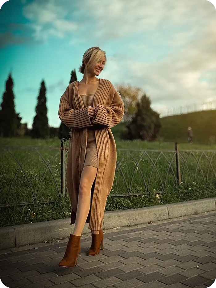 Дівчина в довгому бежевому кардигані на фоні природи