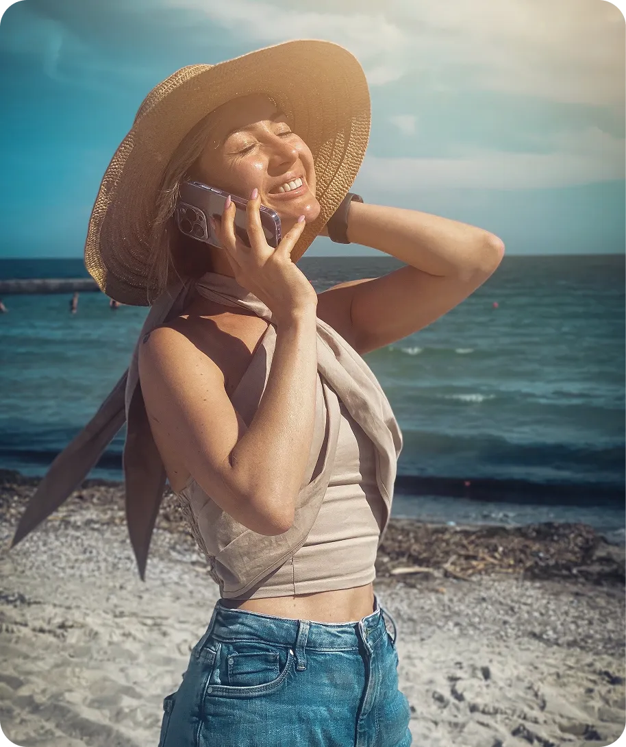 Дівчина на пляжі в капелюсі, розмовляє по телефону
