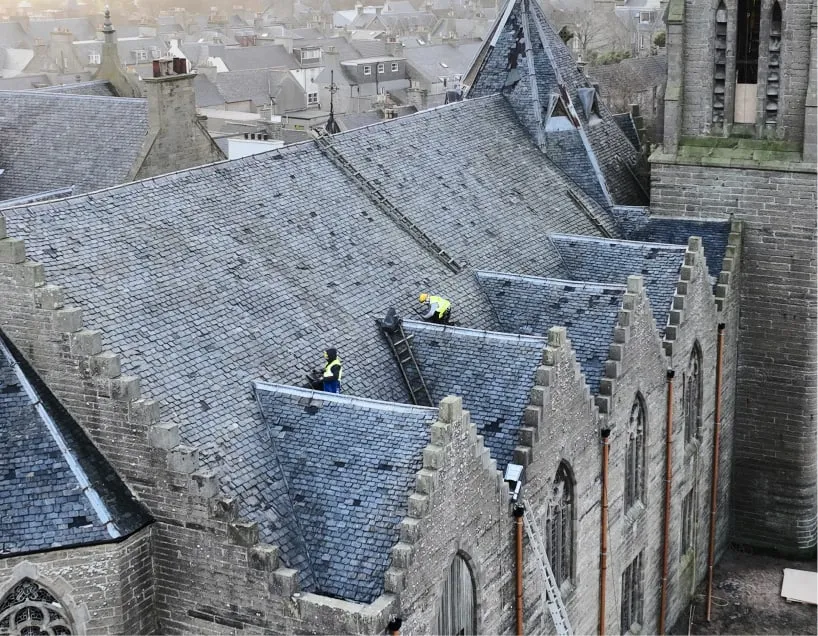 Two roofers in Edinburgh are repairing roof tiles