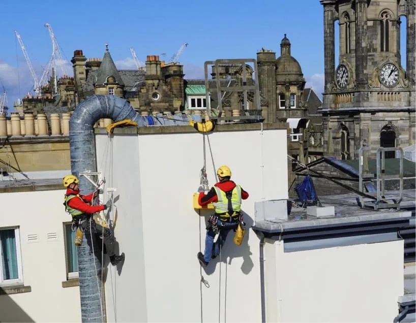 Roofers using rope access to paint the building