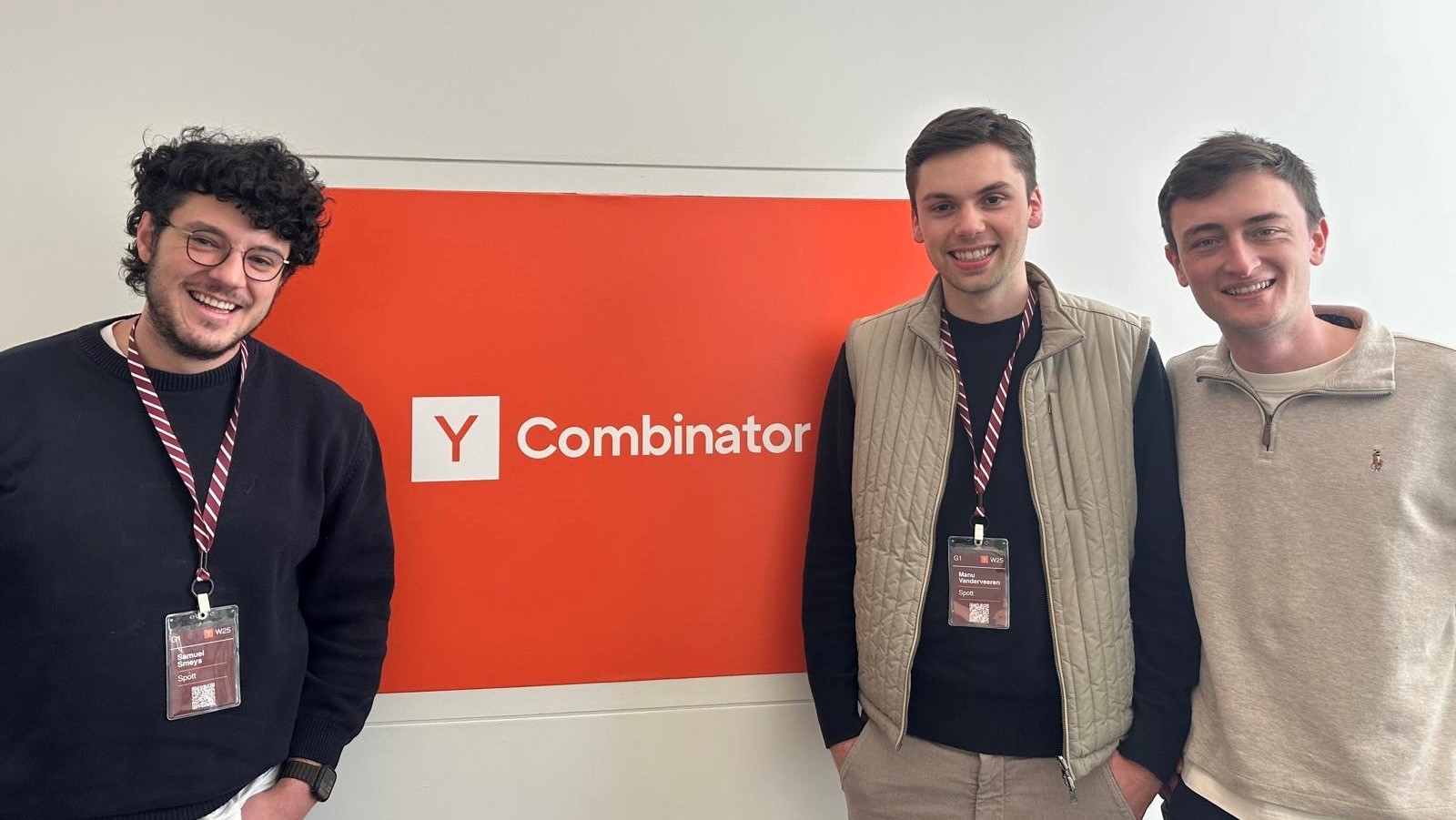 Three smiling young men standing in front of a red and white Y Combinator sign.