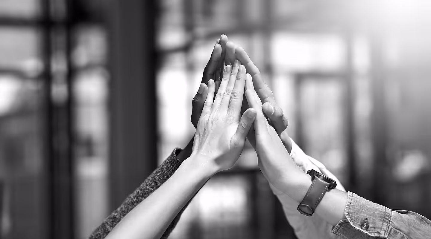 Five diverse hands stacked together in a high-five gesture symbolizing teamwork and unity.