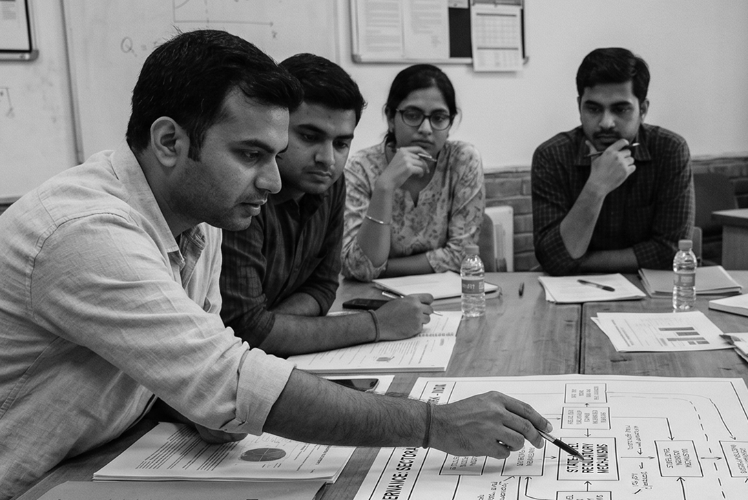 Four people attentively review and discuss documents spread on a table in a meeting room.