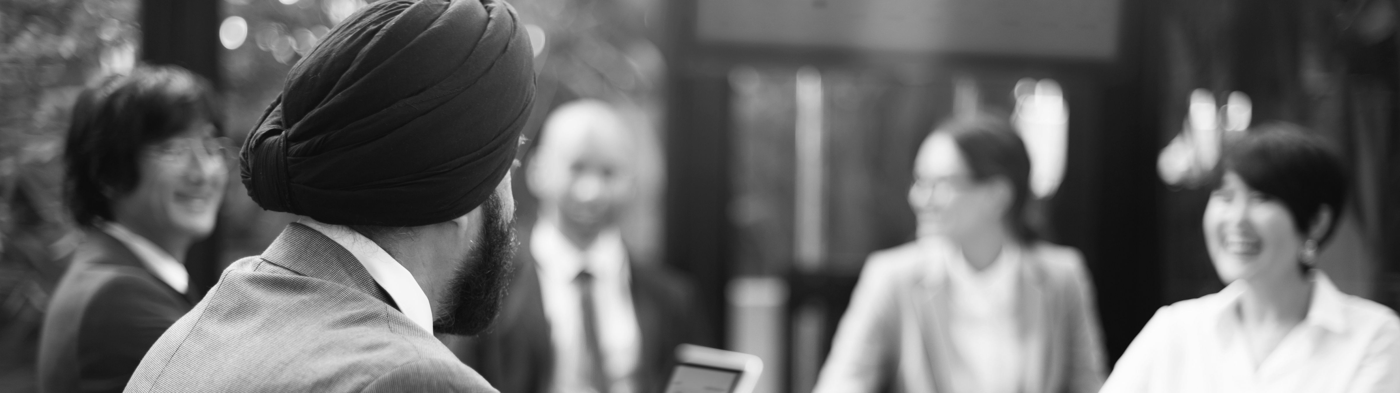 Black and white photo of a diverse group of five professionals engaged in a meeting, smiling and conversing around a table.