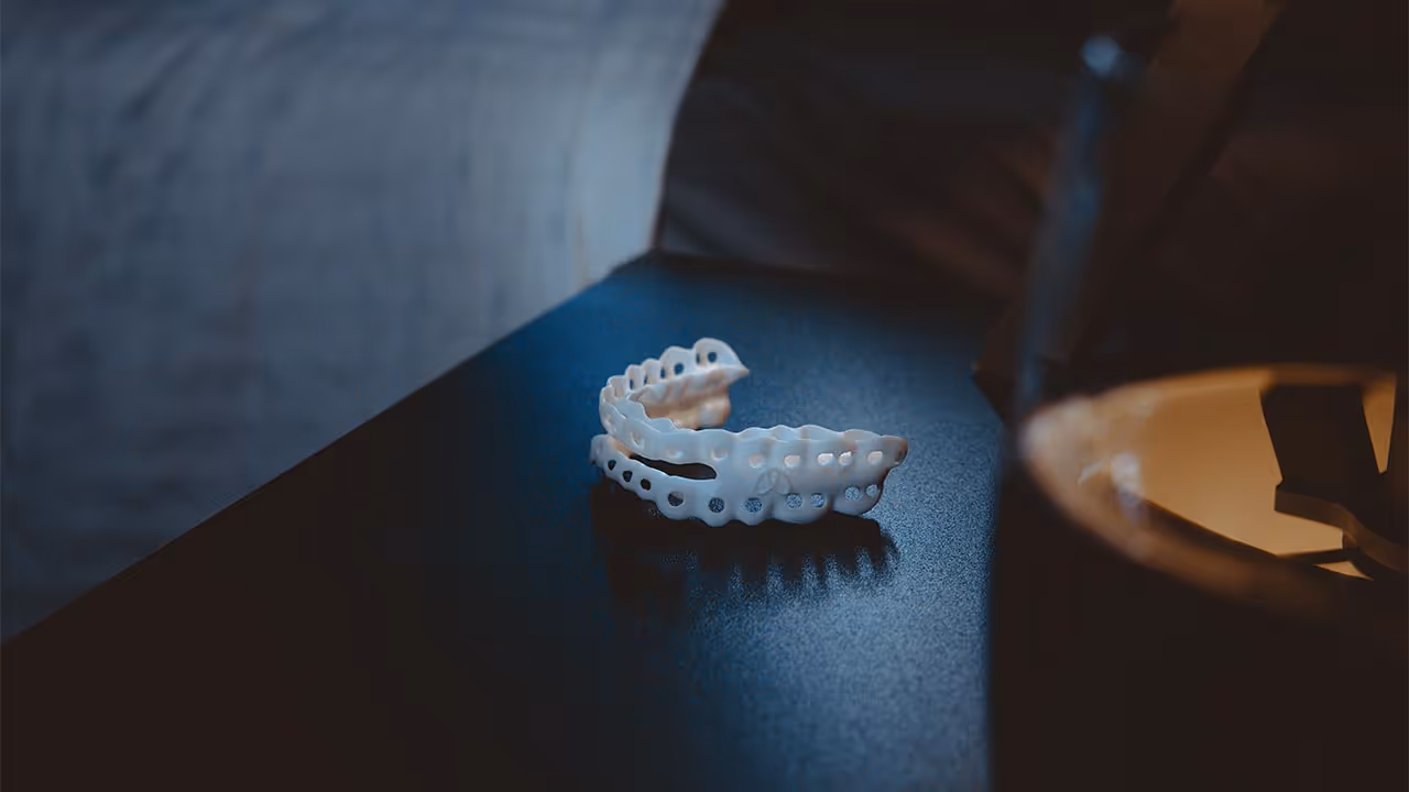 Weisser Zahnschienenaufsatz liegt auf schwarzer Oberfläche vor dunklem Hintergrund.
