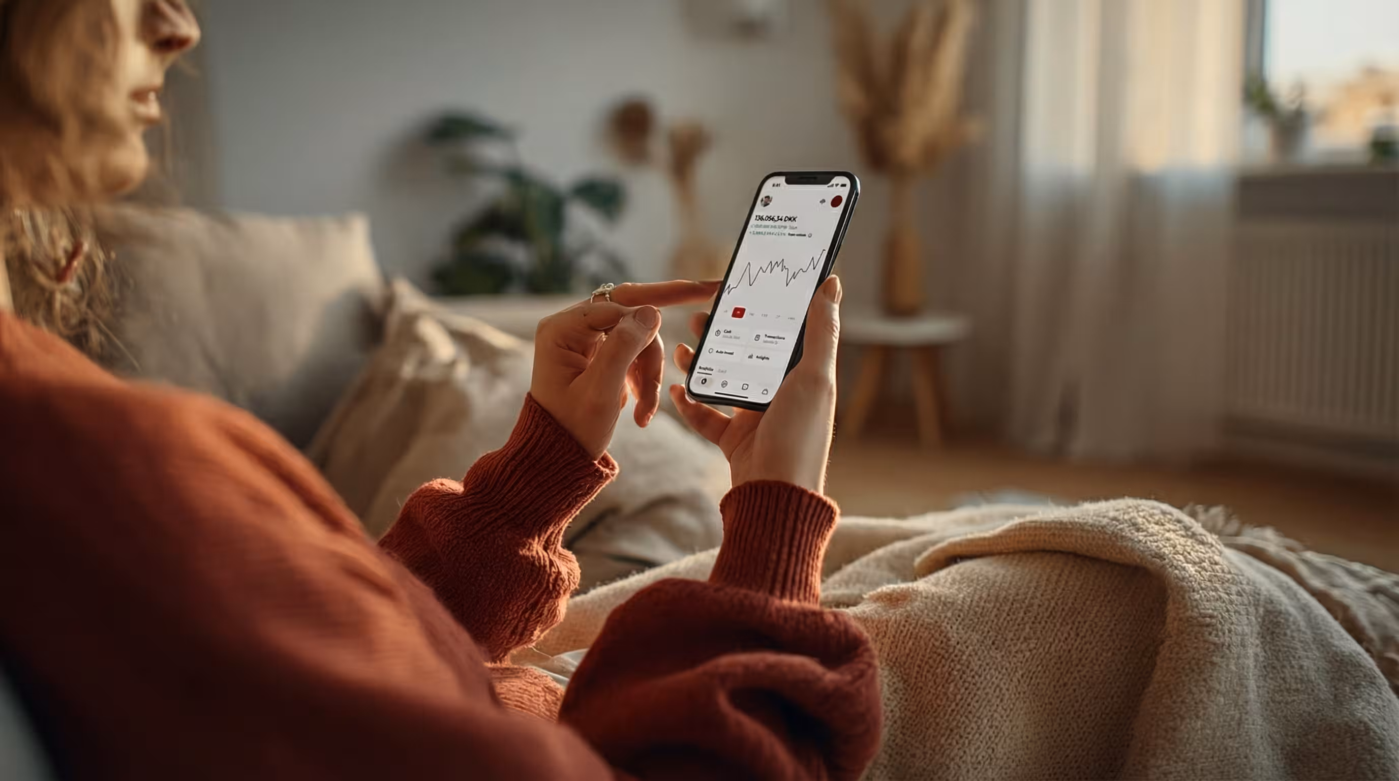 Person in red sweater holding smartphone showing a financial graph on screen.
