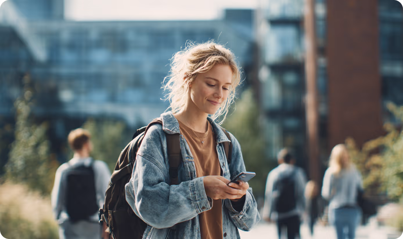 Ung kvinde med rygsæk bruger sin smartphone udendørs på universitetscampus.