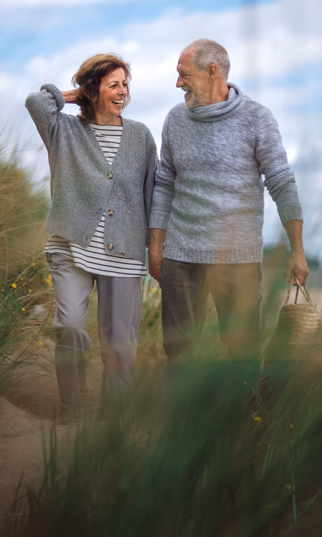 Smiling older couple walking outdoors in gray sweaters, man holding a wicker basket.