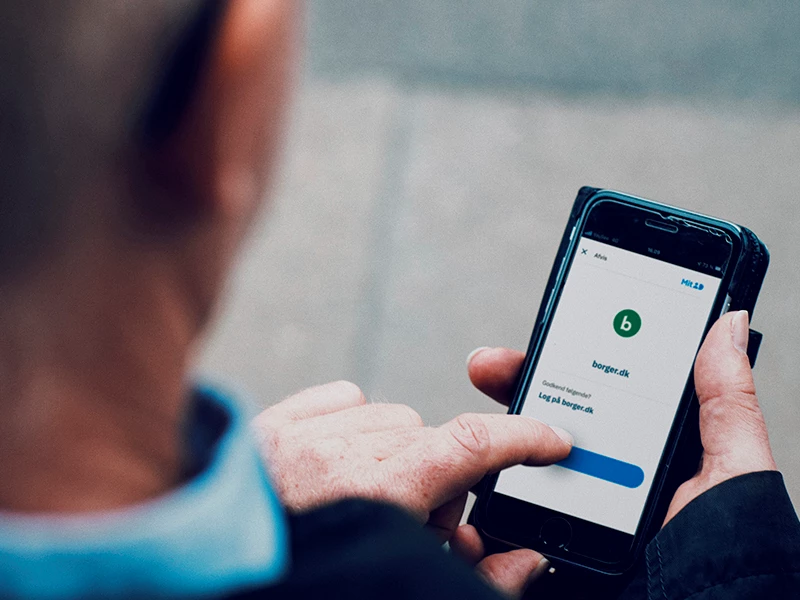 Person holder en smartphone, der viser en godkendelsesknap for borger.dk på skærmen.