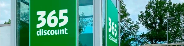 Grøn skilt med teksten 365 discount på en glasbygning omringet af træer.