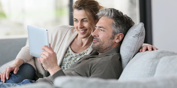 Par smilende, mens de sidder tæt sammen på en sofa og ser på en tablet.