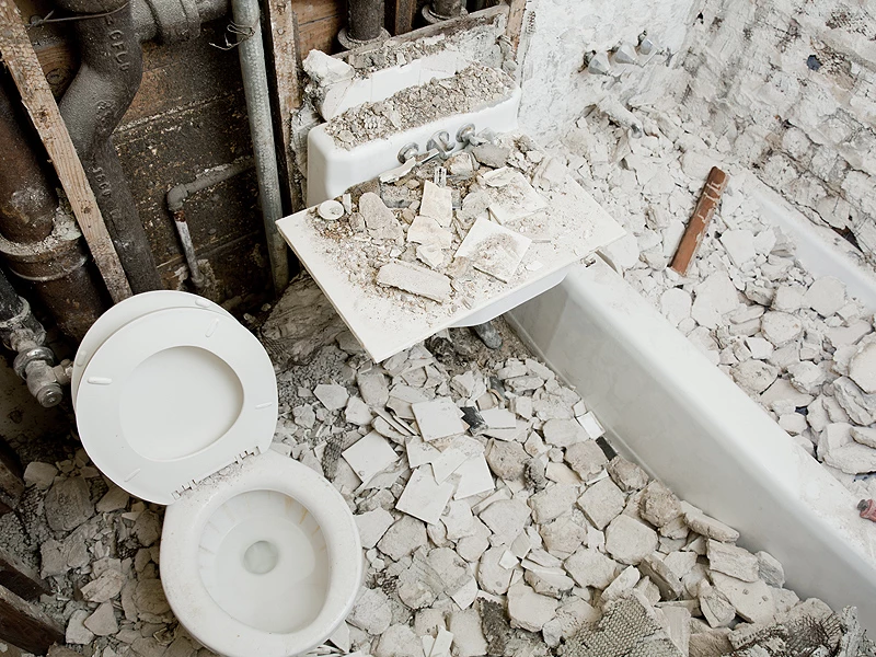 Et badeværelse i ruiner med toilet og vask dækket af murbrokker og snavs.