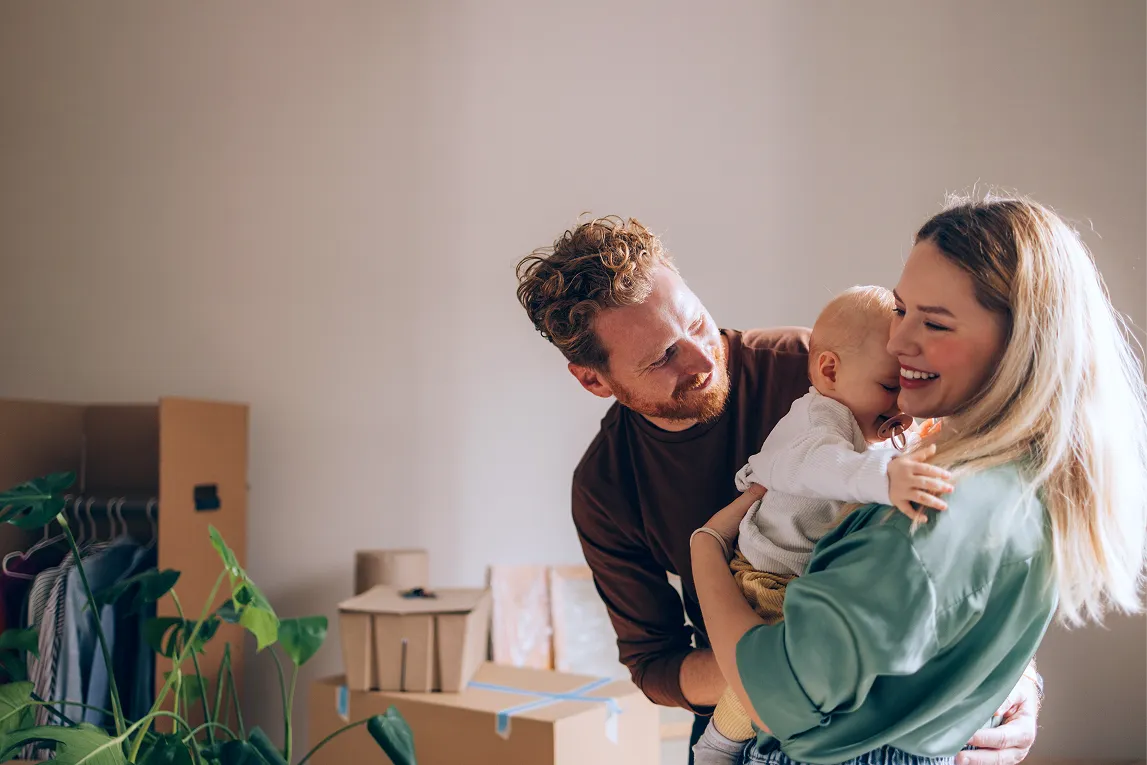 Smilende familie med baby, omgivet af flyttekasser i et nyt hjem.