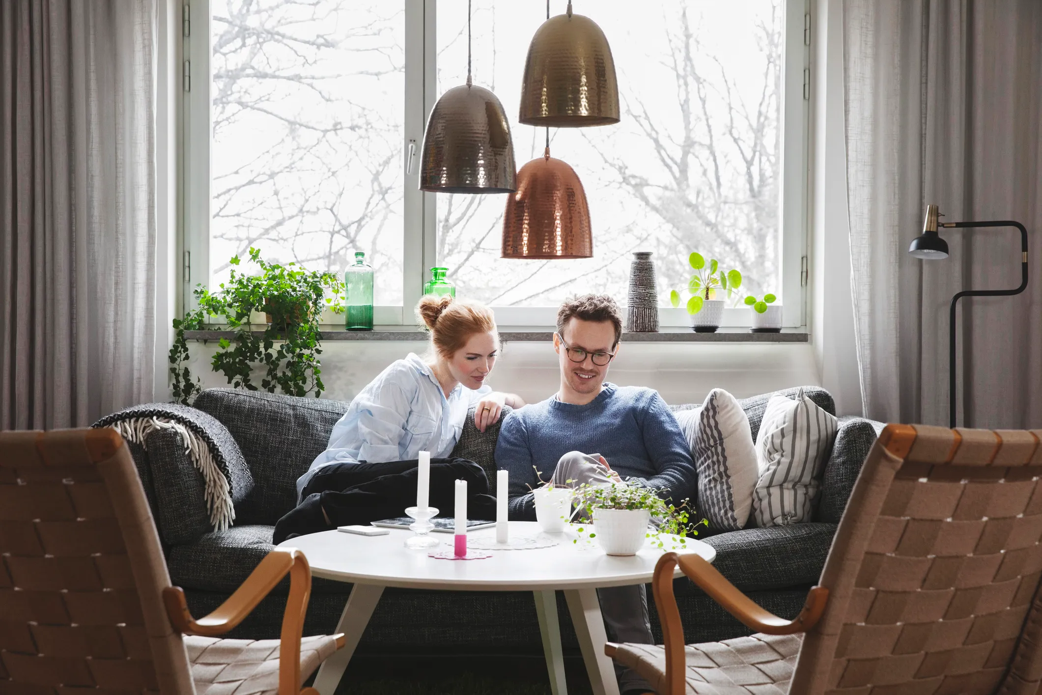 Par sidder tæt sammen på en sofa i en hyggelig stue med planter og hængende lamper.