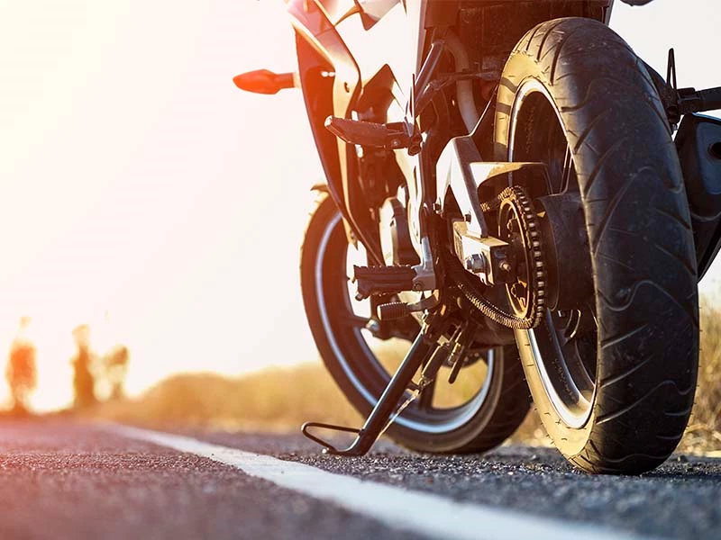 Nedre baghjul og kæde på en motorcykel parkeret på en vej ved solnedgang.
