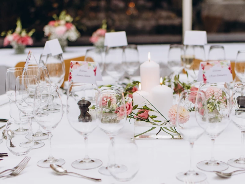Smukt bord dækket med vin- og vandglas, blomsterdekoration og to hvide lys til en fest.