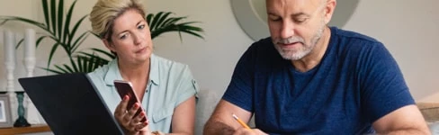 To personer arbejder sammen ved et bord med en bærbar computer og noter.