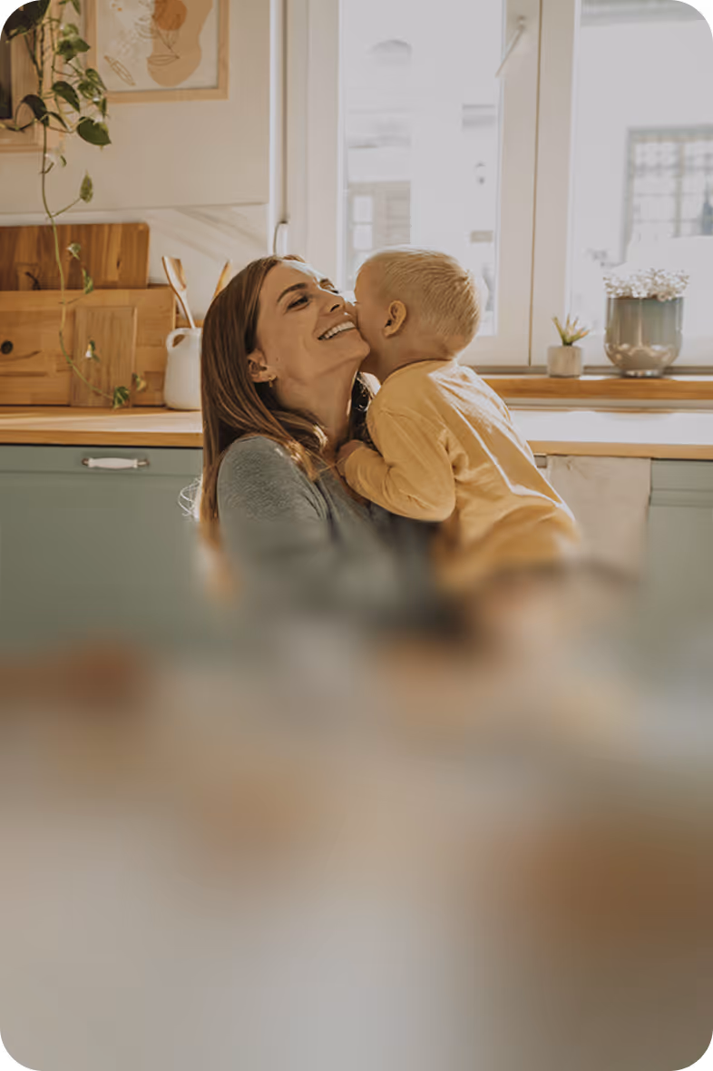 Et barn kysser sin smilende mor i et lyst køkken.